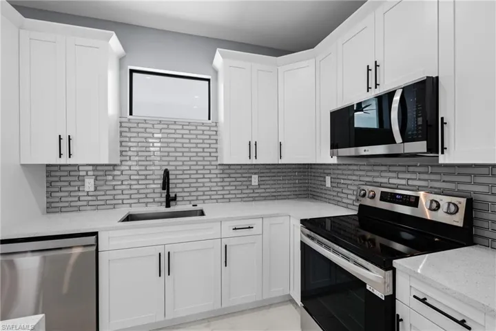 Kitchen featuring sink, white cabinetry, tasteful backsplash, light stone counters, and stainless steel appliances