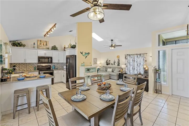 Dining room featuring vaulted ceiling, ceiling fan, light tile patterned flooring, and a skylight