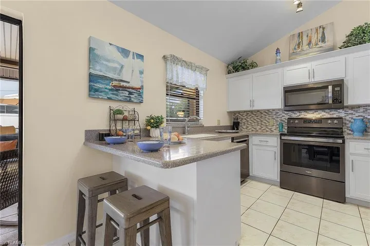 Kitchen featuring stainless steel appliances, a kitchen breakfast bar, white cabinets, a peninsula, and lofted ceiling