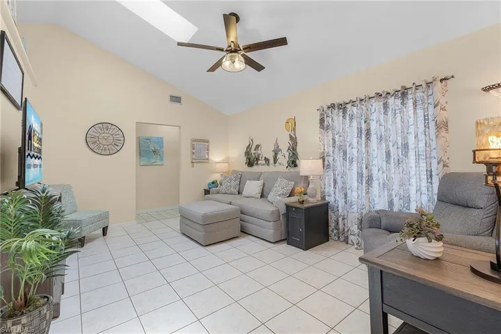 Living room featuring lofted ceiling, ceiling fan, light tile patterned floors, and a skylight