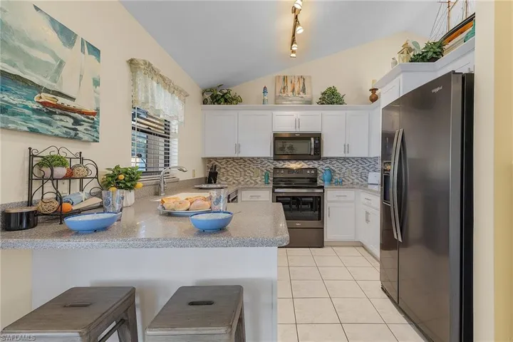 Kitchen featuring stainless steel appliances, a breakfast bar, white cabinetry, lofted ceiling, and a peninsula