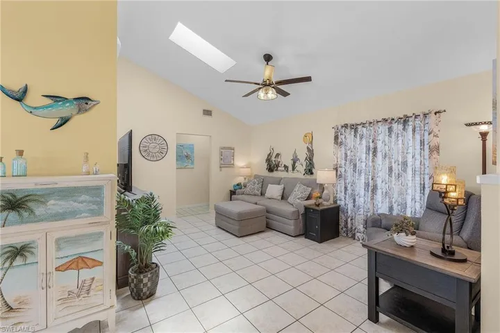 Living room featuring lofted ceiling, a skylight, a ceiling fan, and light tile patterned floors