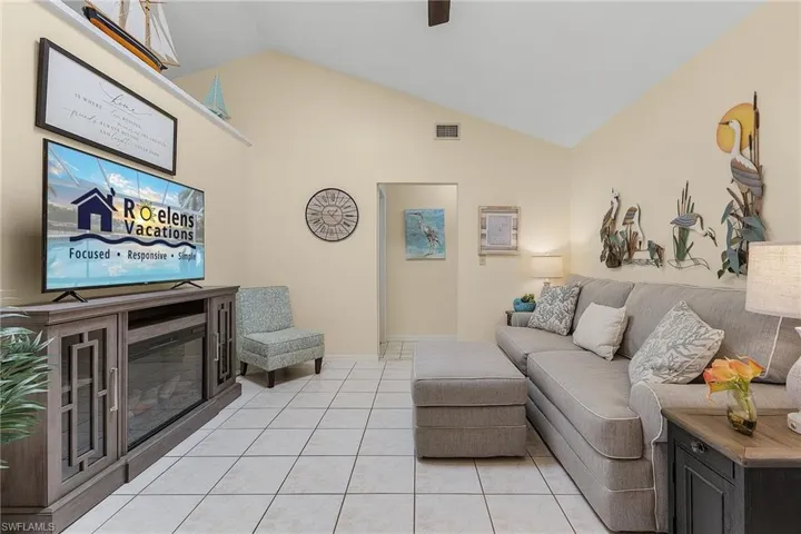 Living area with a glass covered fireplace, lofted ceiling, light tile patterned flooring, and ceiling fan
