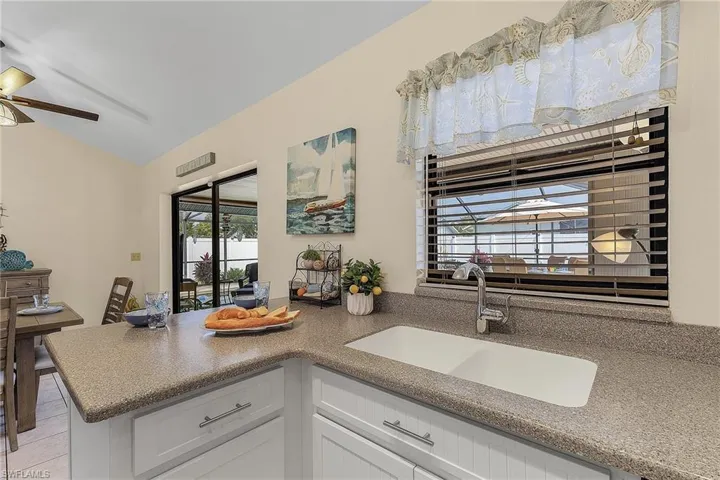 Kitchen featuring a peninsula, vaulted ceiling, white cabinets, ceiling fan, and dark countertops