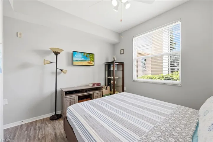 Bedroom featuring wood-finish flooring, a ceiling fan with integrated lighting, a large window with horizontal blinds, and a built-in media console