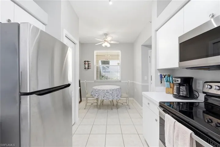 Galley kitchen featuring white cabinetry, stainless steel appliances, light-toned tile flooring, and a window with blinds