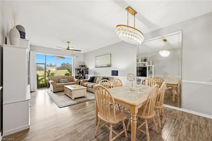 Open-concept living and dining area featuring wood-finish flooring, a full-wall mirror, and a crystal chandelier