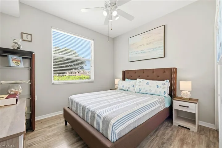 Room featuring wood-finish flooring, a ceiling fan with light fixture, and a large window with blinds