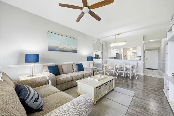 Open-concept living area featuring wood-finish flooring, a contemporary ceiling fan, and a dining space with a decorative chandelier