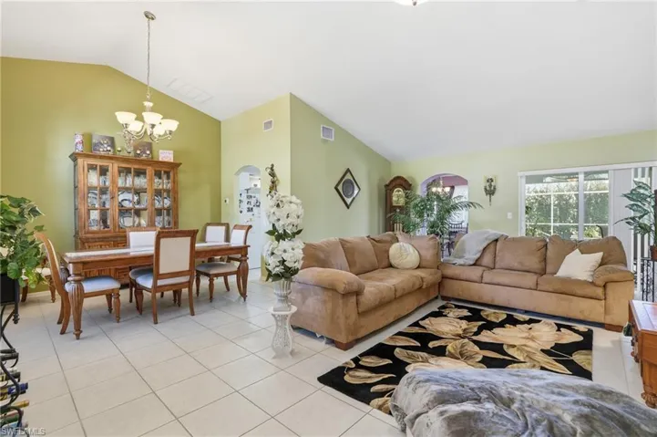 Living area featuring arched walkways, light tile patterned floors, a chandelier, and high vaulted ceiling