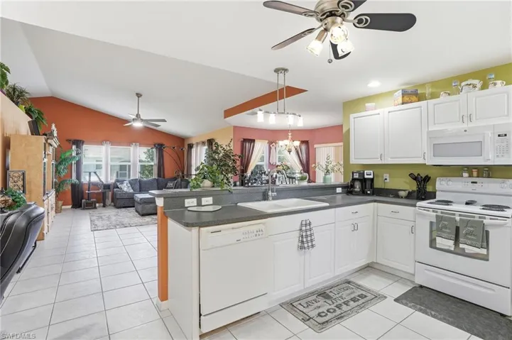 Kitchen featuring white appliances, a ceiling fan, open floor plan, dark countertops, and white cabinets