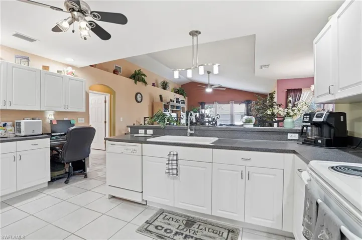 Kitchen with ceiling fan, vaulted ceiling, white cabinetry, dark countertops, and white appliances