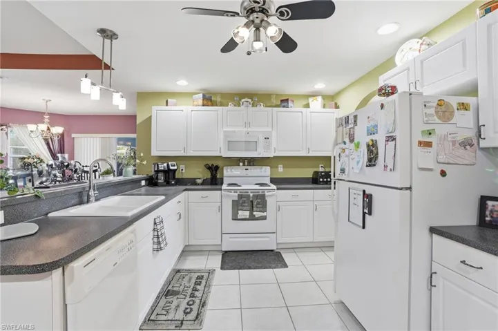 Kitchen featuring dark countertops, white appliances, white cabinets, and light tile patterned flooring