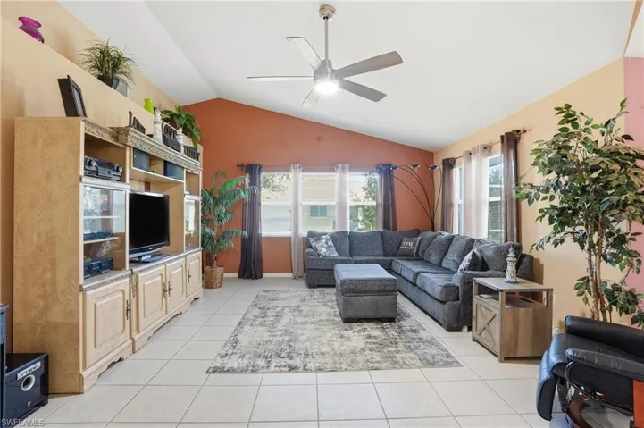 Living area with lofted ceiling, light tile patterned flooring, and a ceiling fan