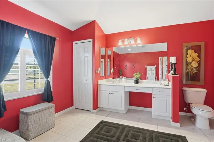 Full bath with vanity, light tile patterned flooring, vaulted ceiling, and a closet