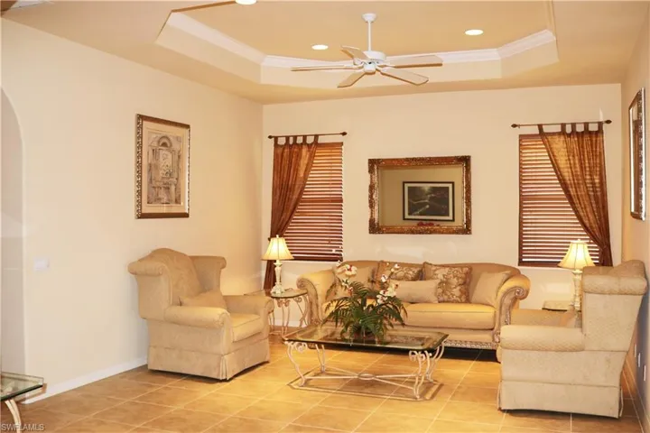 Living area with ornamental molding, a ceiling fan, a raised ceiling and light tile floor