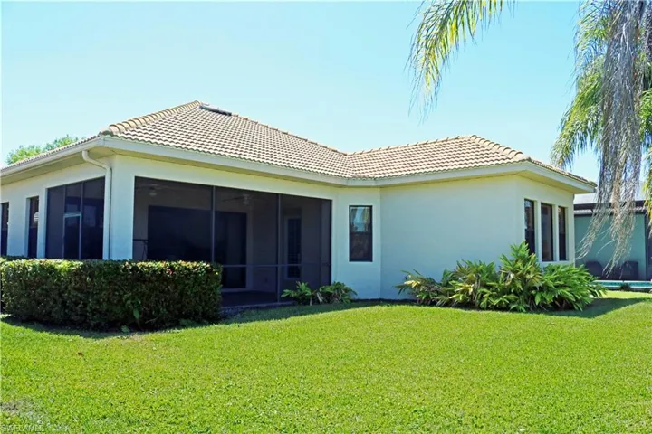 Back of property with a lawn, a tile roof, stucco siding, and screened Lanai