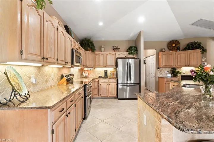 Kitchen with vaulted ceiling, stainless steel appliances, stone counters, tasteful backsplash, and light tile floors