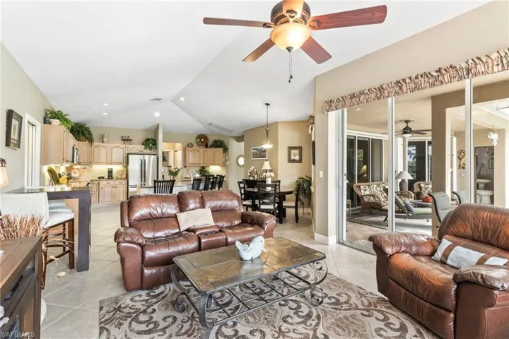 Living room featuring ceiling fan, light tile flooring, and lofted ceiling