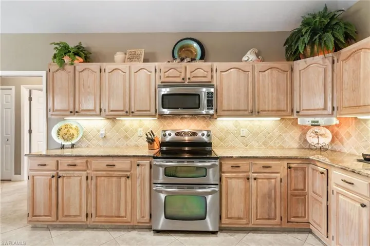 Kitchen featuring light stone countertops, light tile floors, tasteful backsplash, and appliances with stainless steel finishes