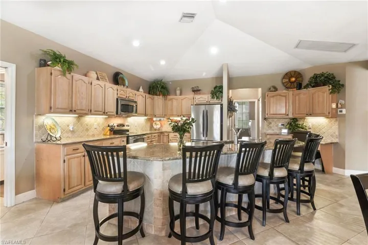 Kitchen featuring appliances with stainless steel finishes, a kitchen island with sink, vaulted ceiling, a breakfast bar, and light tile floors