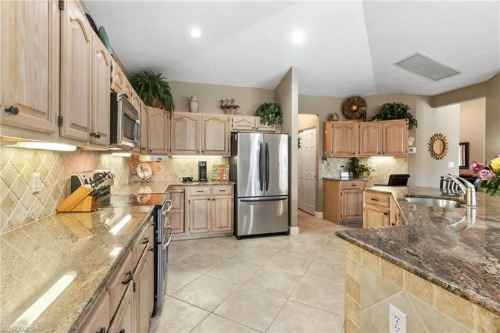 Kitchen with appliances with stainless steel finishes, backsplash, stone counters, sink, and light tile floors