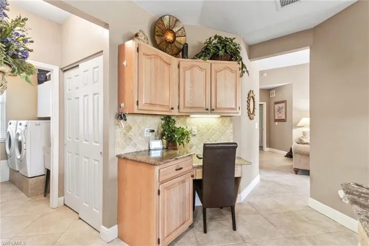 Kitchen with light brown cabinets, light stone counters, light tile flooring, washing machine and clothes dryer, and backsplash