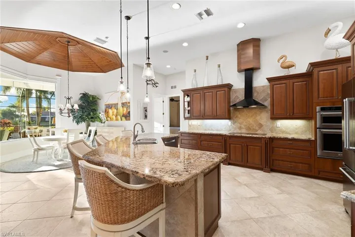 Kitchen with a kitchen bar, hanging light fixtures, tasteful backsplash, light stone counters, and an island with sink