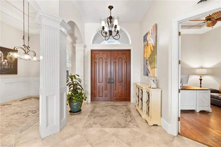 Foyer entrance featuring a chandelier, decorative columns, a decorative wall, arched walkways, and wainscoting