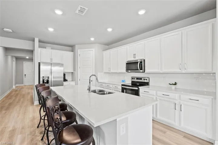 Kitchen with a kitchen breakfast bar, appliances with stainless steel finishes, white cabinets, backsplash, and a kitchen island with sink