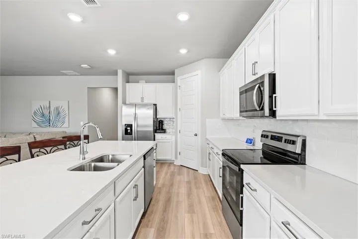 Kitchen with appliances with stainless steel finishes, light vinyl plank flooring, light stone counters, white cabinets, and recessed lighting