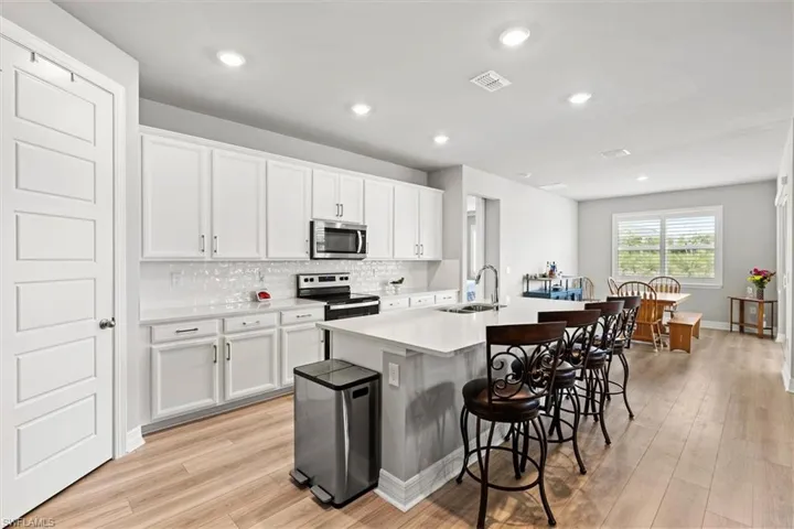Kitchen with white cabinetry, an island with sink, stainless steel appliances, a breakfast bar, and backsplash