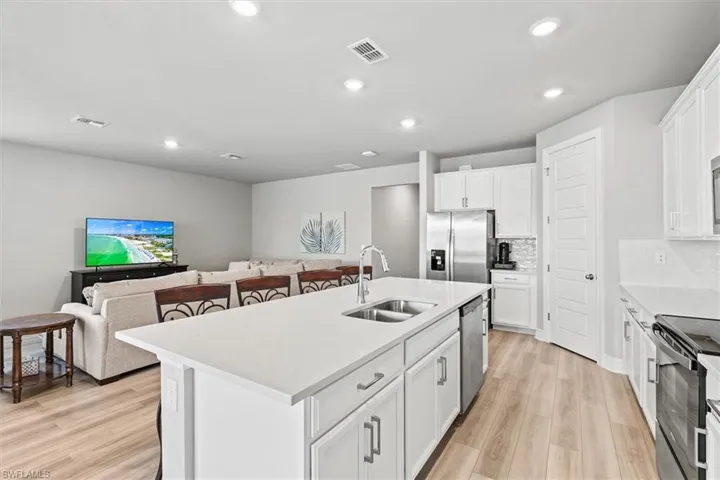 Kitchen with stainless steel appliances, white cabinets, open floor plan, light vinyl plank floors, and recessed lighting