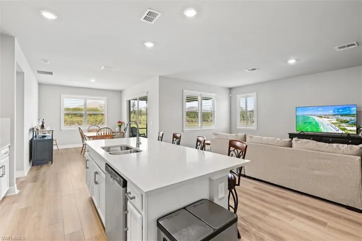 Kitchen featuring light vinyl plank flooring, open floor plan, white cabinetry, a breakfast bar area, and light stone counters