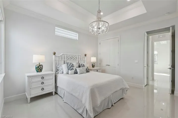 Bedroom featuring baseboards, a tray ceiling, ornamental molding, a closet, and a notable chandelier