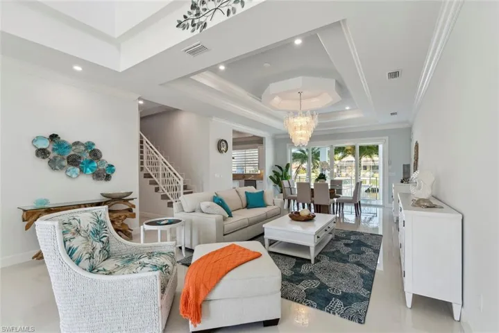 Living room featuring visible vents, a chandelier, stairs, ornamental molding, and a raised ceiling