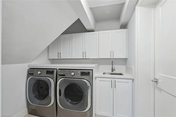 Laundry area featuring independent washer and dryer, a sink, wet bar, cabinet space, and baseboards
