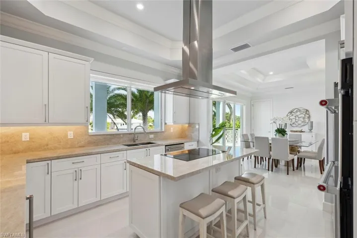 Kitchen featuring visible vents, a tray ceiling, a sink, black electric stovetop, and island range hood