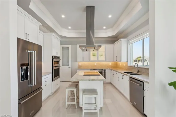 Kitchen featuring a sink, appliances with stainless steel finishes, a raised ceiling, backsplash, and a center island