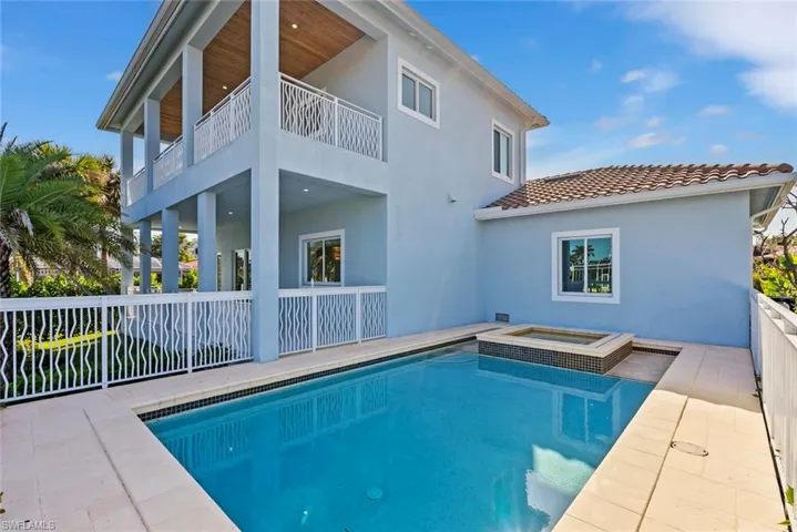 Back of property with a balcony, a pool with connected hot tub, stucco siding, a tile roof, and a patio area