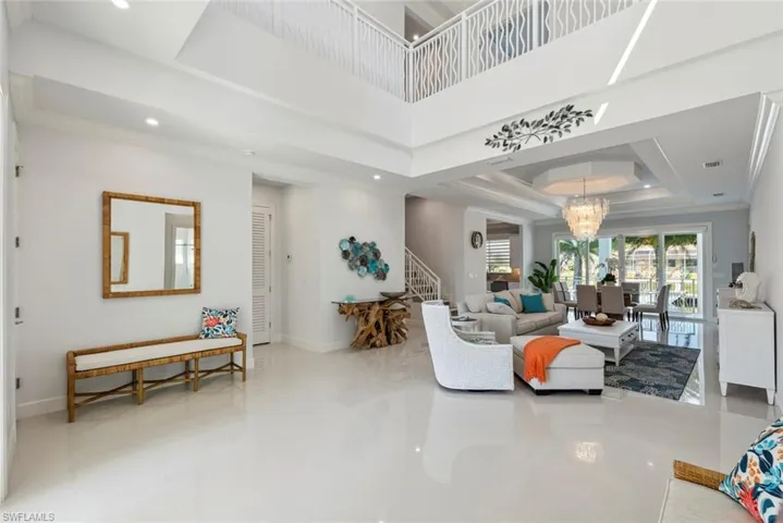 Living room with a raised ceiling, stairway, an inviting chandelier, crown molding, and baseboards