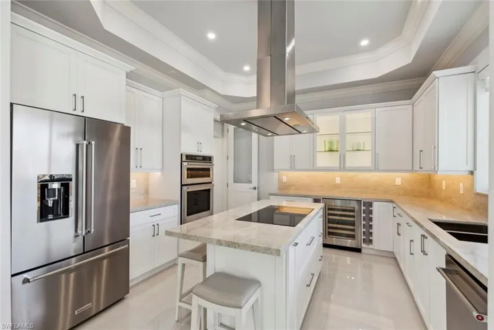 Kitchen featuring a kitchen island, wine cooler, a tray ceiling, appliances with stainless steel finishes, and island range hood