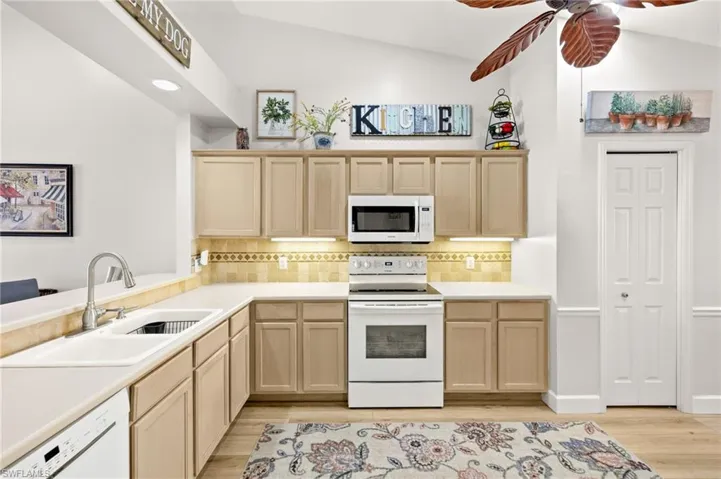 Kitchen with white appliances, light brown cabinetry, light wood finished floors, decorative backsplash, and lofted ceiling
