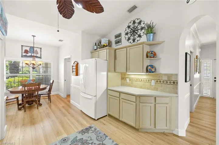 Kitchen with freestanding refrigerator, cream cabinets, tasteful backsplash, arched walkways, and light wood-type flooring