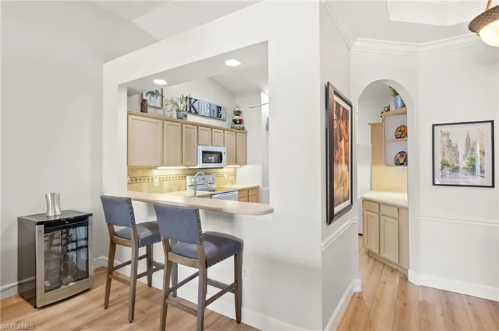 Kitchen with white appliances, beverage cooler, light countertops, light wood-style floors, and a kitchen breakfast bar