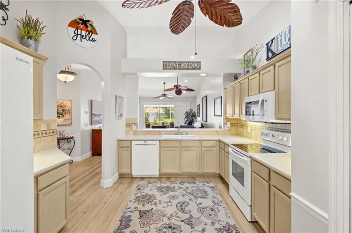 Kitchen featuring white appliances, a ceiling fan, tasteful backsplash, light wood finished floors, and light countertops
