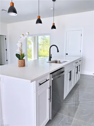 Kitchen with a kitchen island with sink, decorative light fixtures, light stone countertops, dishwasher, and white cabinetry