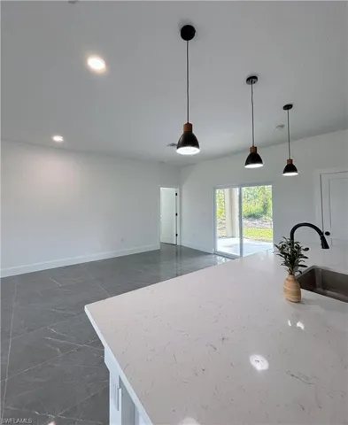 Kitchen with a sink, baseboards, recessed lighting, decorative light fixtures, and light stone countertops
