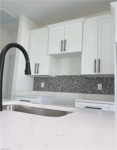 Kitchen featuring white cabinetry, light stone counters, tasteful backsplash, and a sink