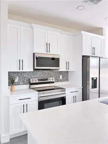 Kitchen featuring appliances with stainless steel finishes, white cabinets, and a textured ceiling